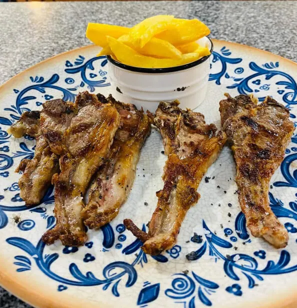 Chuletillas de cordero con patatas fritas en un plato azul y blanco.