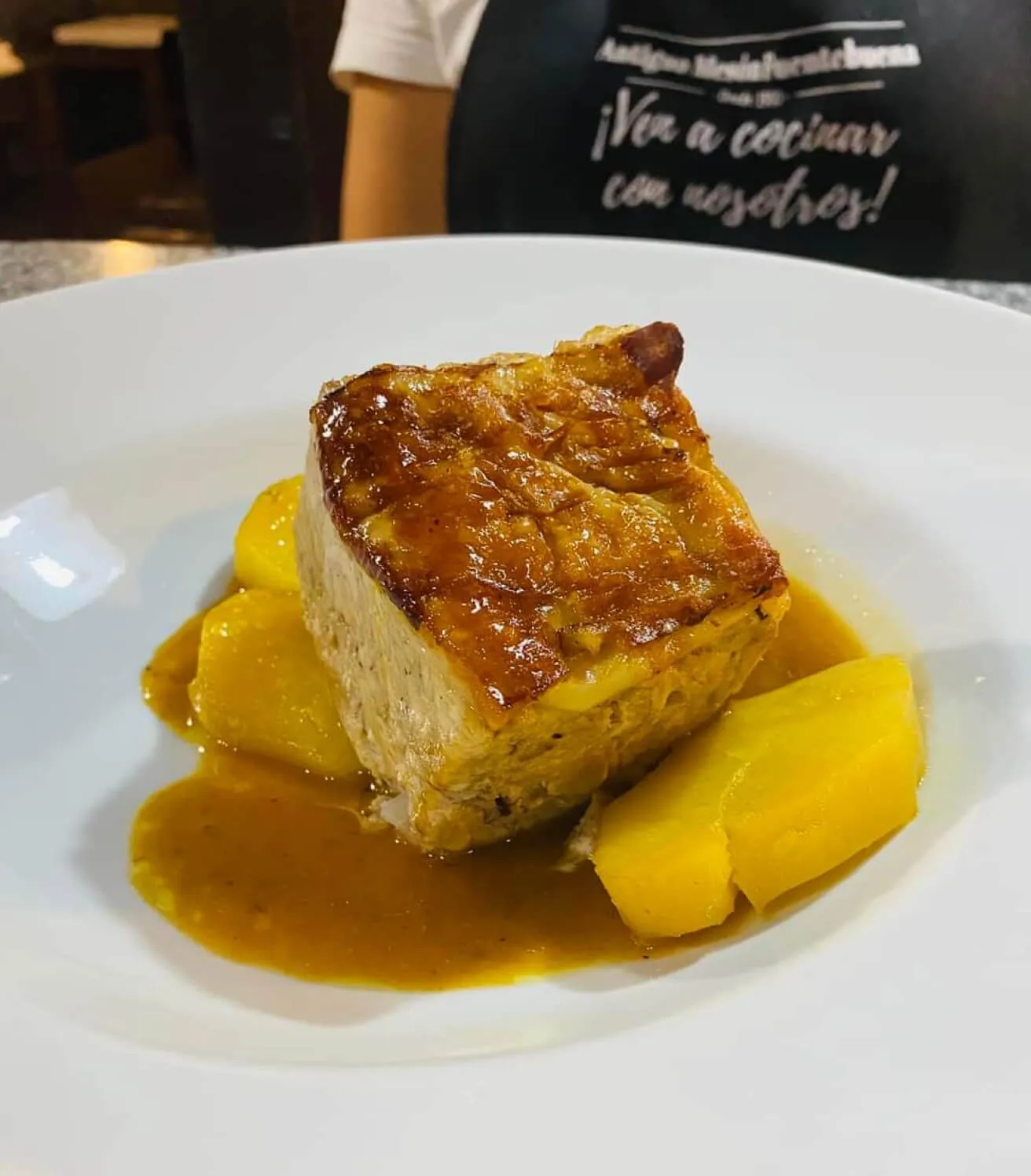 Un plato con cochinillo a la brasa, salsa y patatas.