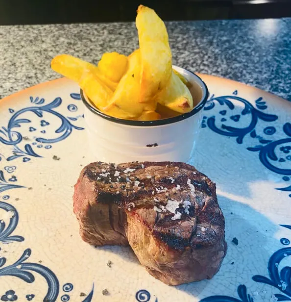 Un medallón de solomillo de ternera y papas fritas en un plato azul y blanco.