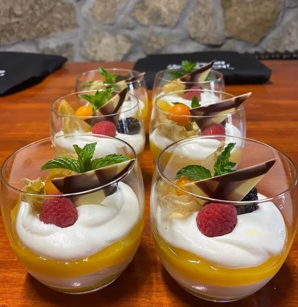 Cuatro vasos llenos de postre de mango y queso encima de una mesa de madera.